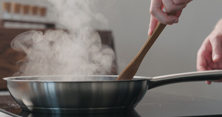 man hand moving something with wooden spatula in fry pan