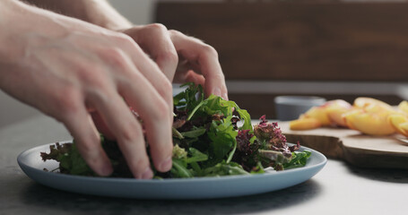 man making salad with nectarines and mozzarella on a blue plate on concrete countertop on kitchen, add greens