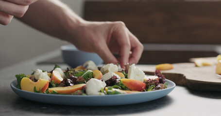 man making salad with nectarines and mozzarella on a blue plate on concrete countertop on kitchen, add mozzarella