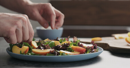 man making salad with nectarines and mozzarella on a blue plate on concrete countertop on kitchen, add nectarines