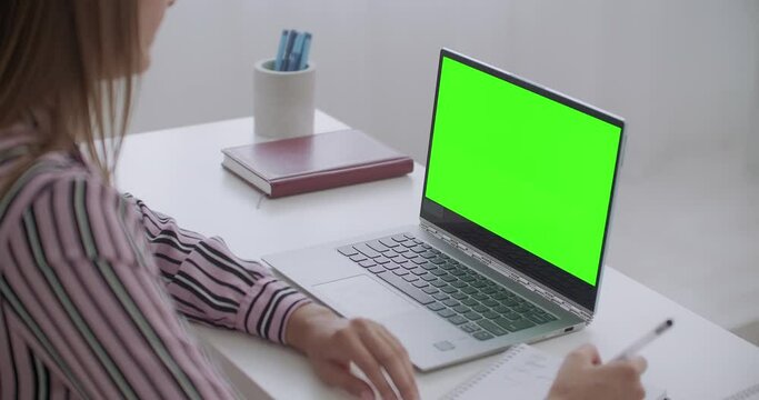 e-education, woman is viewing on laptop with green screen for chroma key technology, female student is writing notes