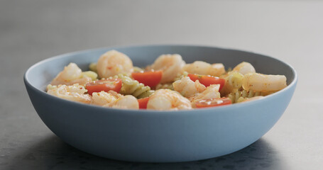 pesto fusilli pasta with shrimps and cherry tomatoes in blue bowl on concrete background