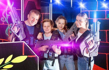 Modern young parents and children with laser pistols posing together in a dark laser tag labyrinth