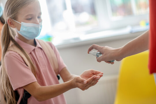 Girl In Preventive Mask Disinfecting Her Hands While Enetering The School