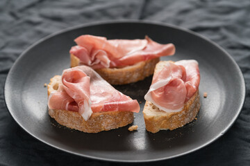 ciabatta with thin prosciutto on black plate on linen background