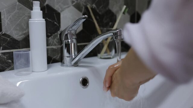 Crop faceless woman washing hands in sink in bathroom in morning while doing everyday hygiene treatment 