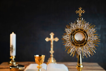 Fototapeta na wymiar Catholic religion concept. Catholic symbols composition. The Cross, monstrance, Holy Bible and golden chalice on wooden altar. 