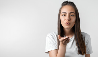 Beautiful young woman makes air kiss, blows over palm. Studio shot, white background. Copy space