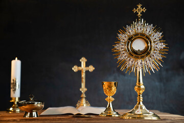 Catholic religion concept. Catholic symbols composition. The Cross, monstrance,  Holy Bible and golden chalice on wooden altar.  - obrazy, fototapety, plakaty