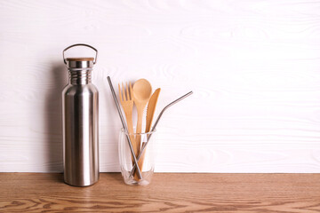 Eco set with bamboo cutlery, reusable water bottle on wooden background.