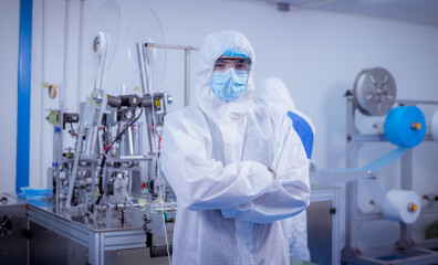 Technician worker wearing protective suite , glove are inspect machine with check  face mask manufacturing process to safe and against from virus.