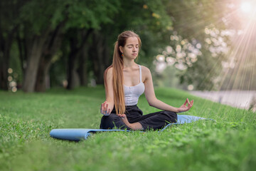 portrait of a young woman practicing yoga in the park on the grass, lotus position, relaxation and meditation concept