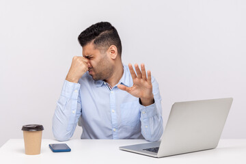 Displeased male employee confused by bad smell in office workplace, holding breath pinching his nose