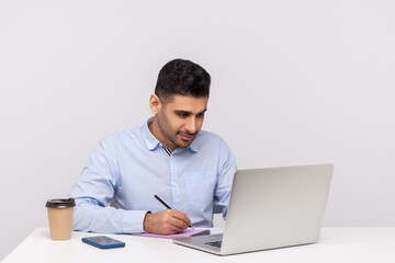 Busy man employee working on laptop and writing paper notebook, preparing report doing paperwork