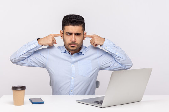 Can't Hear This Anymore! Annoyed Man Employee Sitting At Workplace, Covering Ears And Frowning Angry Displeased