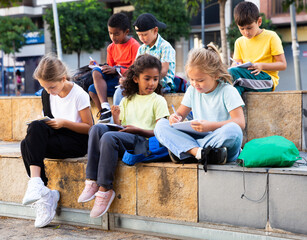 International group of interested tweenagers studying outside school, writing in workbooks. Back...