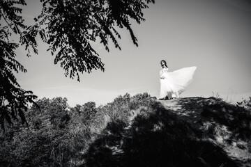 Fototapeta premium Black and white photo bride in a white dress posing on a hill against the sky.