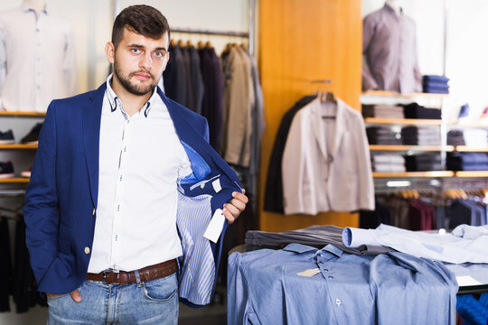 Young man customer choosing fashion jacket in men shop.