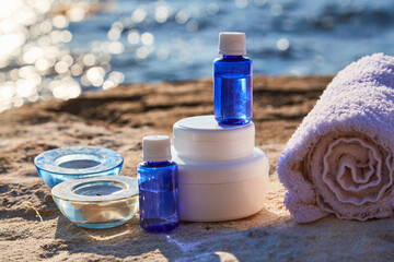 Obraz na płótnie Canvas Bottles with aroma oils and glass candles on rock. Towel and containers with cream. Spa treatment and relax near sea
