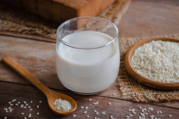 Sesame milk in glass and white sesame seeds on wooden spoon