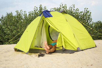        View of legs with bare heels protruding from a yellow tent mounted on the sand.