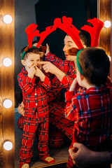 Happy family in red pajamas. Father with little son grimace in the mirror.