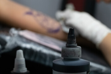 Tattoo concept. A jar of paint for tattoos, stands against the background of a man's hand. You can also see how the master fills the pattern on the forearm.