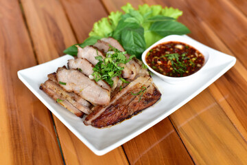 Thai Food Grilled Pork with Thai or Charcoal-boiled Pork Neck with the Sauce is Spicy Sour Taste in a white plate on a wooden table is a Popular Appetizer in Thailand.