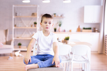 child in a white T-shirt and jeans sits on a chair