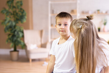 Little sister plays with her brother. Cute girl and boy are sitting at home.