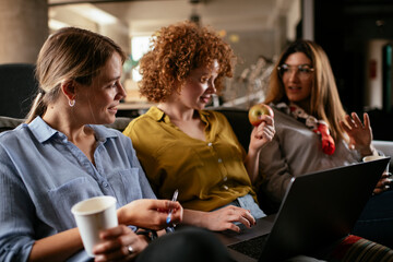 Girlfriends talking and laughing in office. Beautiful women drinking coffee in the office.