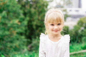 beautiful little blonde girl in white blouse smiling outdoors. copy space to the left