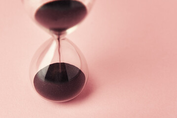 Hourglass on pink background, closeup. Urgency and running out of time concept
