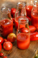 Fototapeta na wymiar Tomato juice in glass bottle and fresh tomatoes on a wooden table close up view