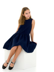 Naklejka premium Charming Blonde Girl in Dress Sitting on White Cube Looking Up