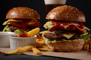 Homemade burger with grilled beef, cheese, onion, tomato, and green salad, sauce, with pickles and French fries