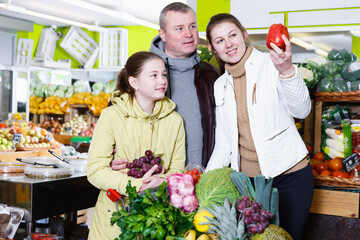 Naklejka premium Happy family with preteen daughter in search of fresh apples in fruit store