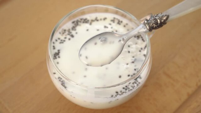 Chia seeds in kefir cocktail in dessert spoon and glass cup on wooden brown board close up