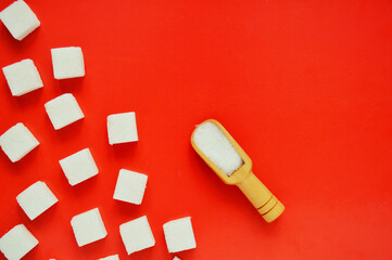 Refined sugar and wooden spoon with loose sugar on red background.