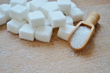 Refined sugar and wooden spoon with loose sugar on wooden background.