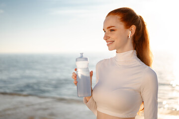 Image of redhead joyful sportswoman drinking water while working out