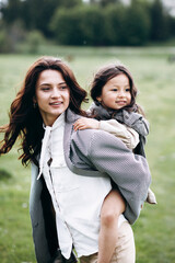 Stylish mother and daughter have fun outdoors in a field with green grass by the river when it rains