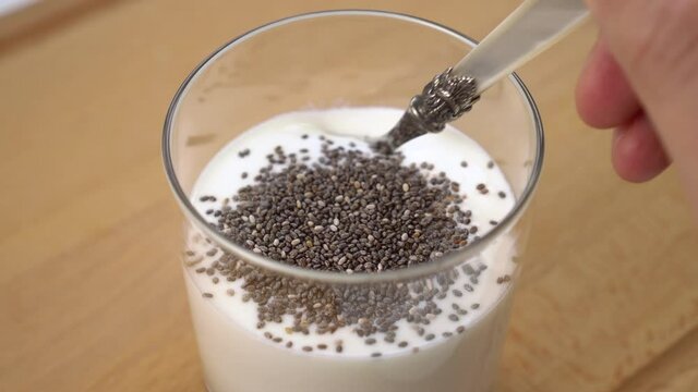 Mixing kefir or yogurt with chia seeds in a glass on a wooden cutting board. Making a Healthy Cocktail. Close up