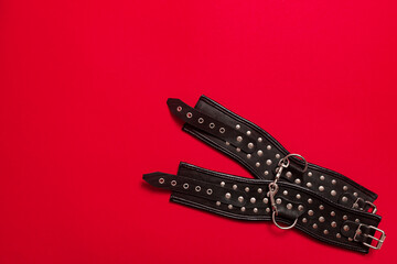 Red color banner with black leather bracers and metal rivets for shackling hands or legs and performing sexual games. BDSM subject. Background for advertising adult products and sex toy store