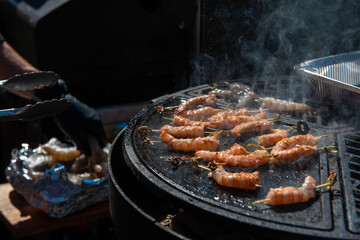 A professional cook prepares shrimps on the grill outdoor, food or catering concept