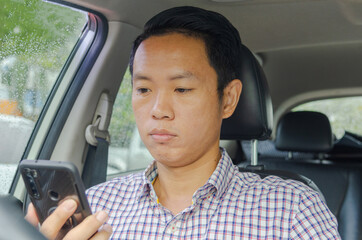 Asian man wearing a plaid shirt looks at his phone in a car.