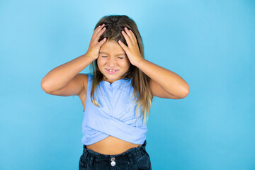 Young beautiful child girl over isolated blue background suffering from headache desperate and stressed because pain and migraine with her hands on head