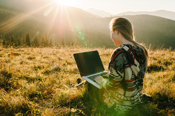 Hipster woman working with laptop sitting in mountains. Hiker tourist enjoying valley view sunset....