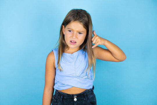 Young beautiful child girl over isolated blue background confused doing phone gesture with hand and fingers like talking on the telephone
