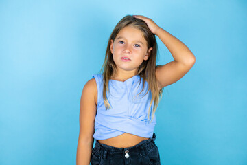 Young beautiful child girl over isolated blue background putting one hand on her head smiling like...